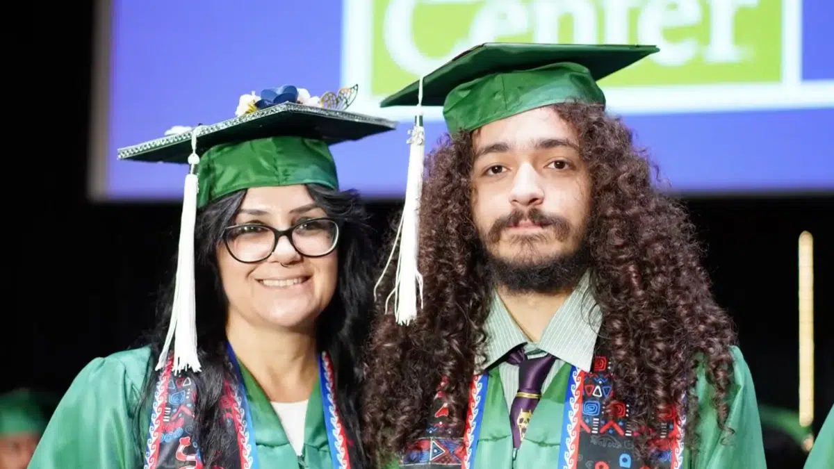 Melody and Cecil Carrizosa in green graduation caps and gowns smiling together
