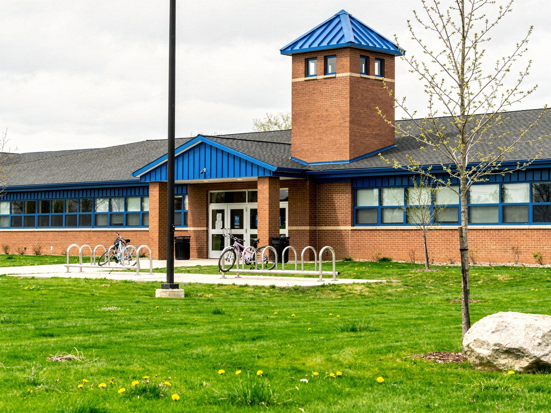 Single-story brick school building with a blue-roofed tower and bikes out front