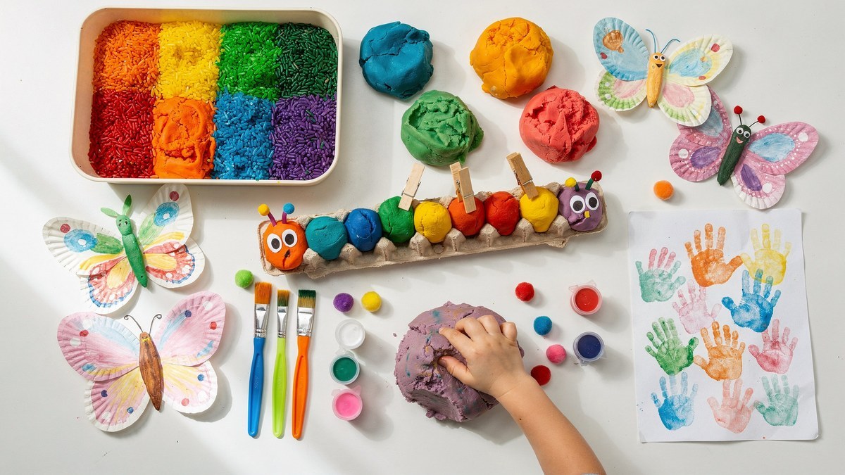 Preschool craft table with rainbow sensory rice, play dough, an egg-carton caterpillar, paper-plate butterflies and a handprint painting