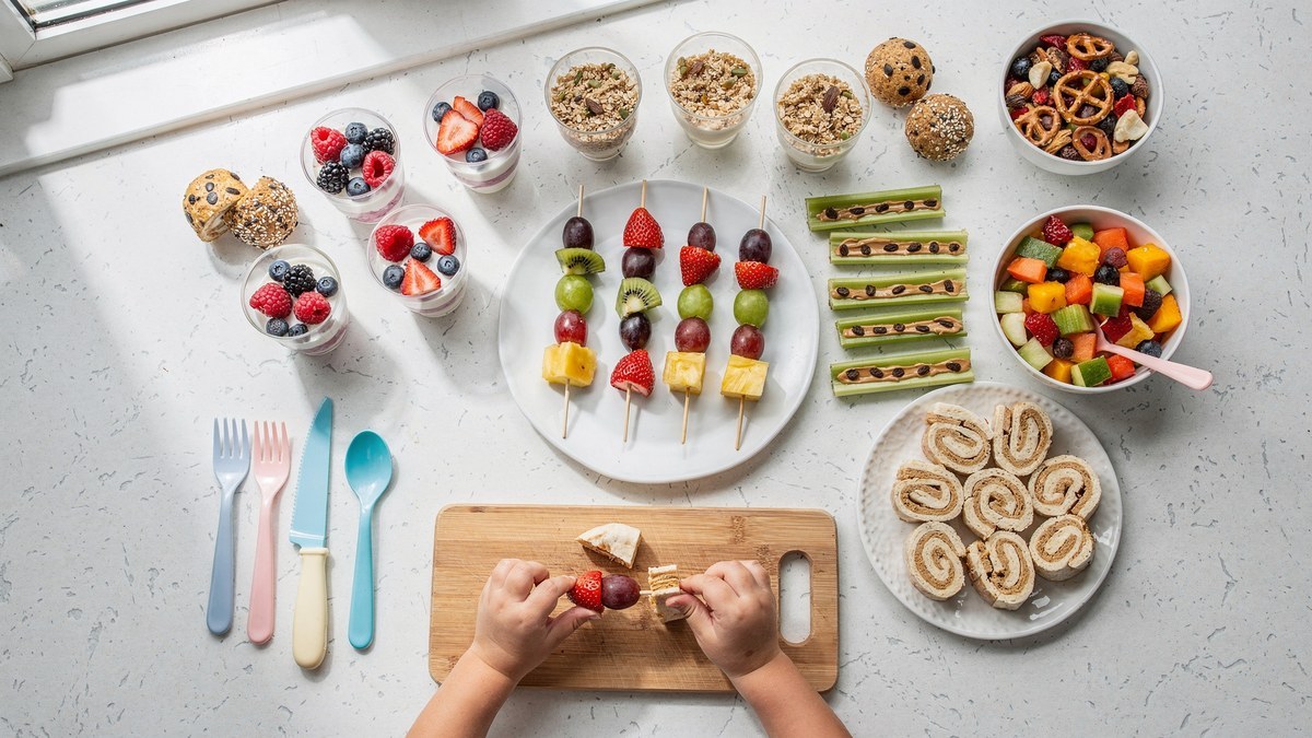 No-bake snacks for preschoolers: fruit skewers, yogurt parfaits, ants on a log, pinwheel roll-ups, energy bites and trail mix, with small hands threading fruit