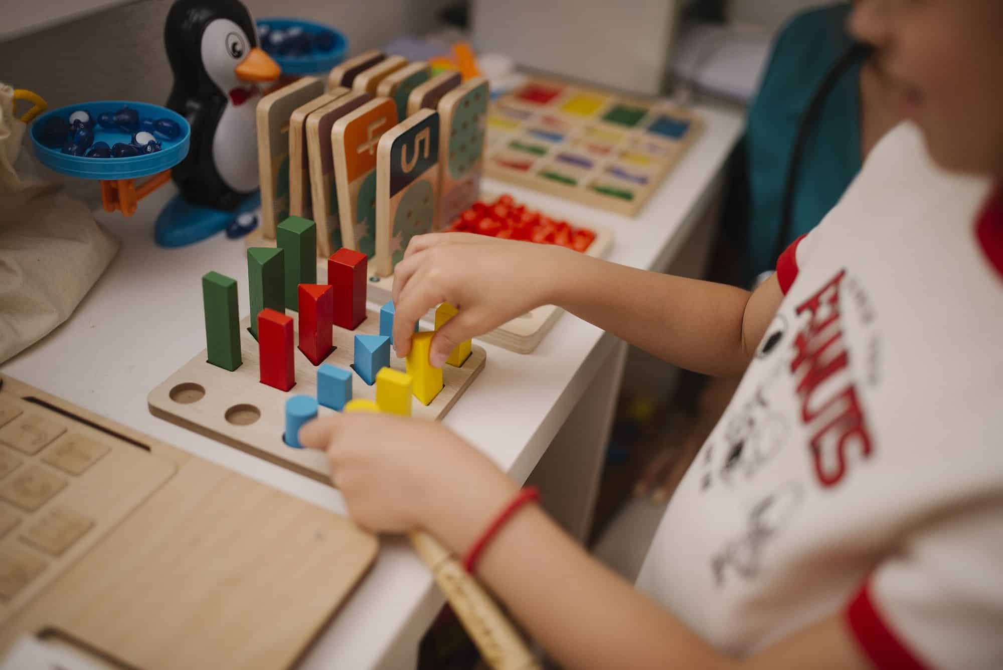 New Hampshire Requires Play in Kindergarten. Teachers Say Benchmarks Are Squeezing It Out. 6 A young child's hands stacking and sorting colorful wooden blocks and shapes on a table