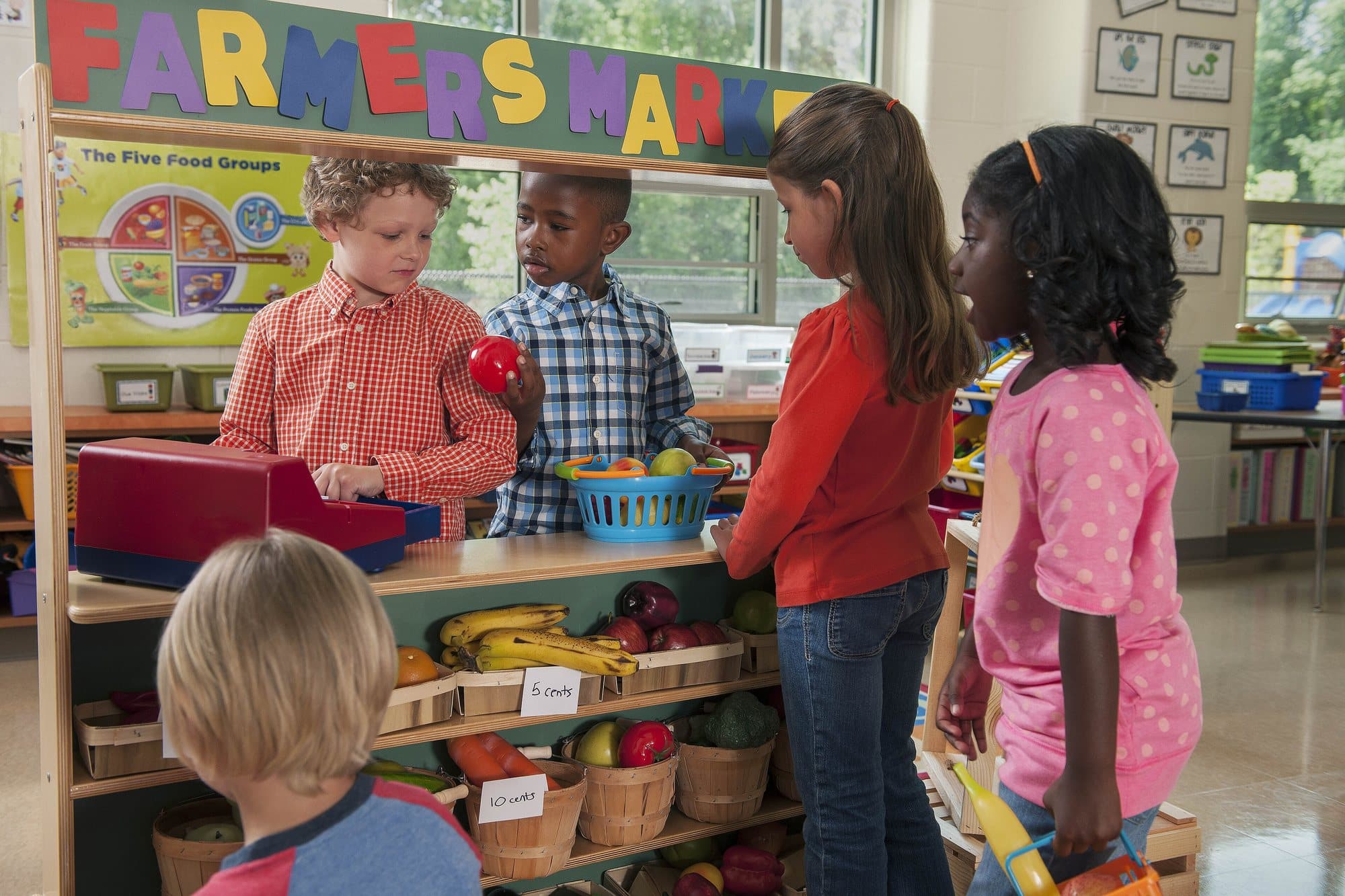 New Hampshire Requires Play in Kindergarten. Teachers Say Benchmarks Are Squeezing It Out. 5 Kindergarteners playing at a pretend farmers market stand in a classroom dramatic play center