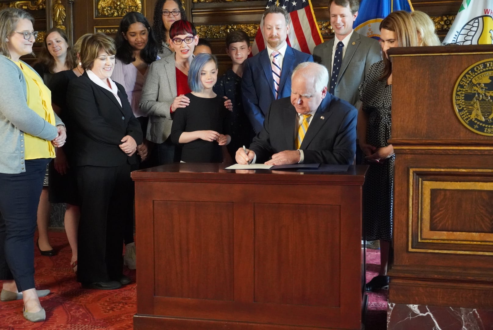 Minnesota Gov. Tim Walz signs an education bill at a ceremonial bill signing surrounded by supporters